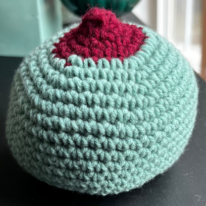 One extra-large, mint green crocheted breast model with a large red, perky nipple to teach latching and breastfeeding education.